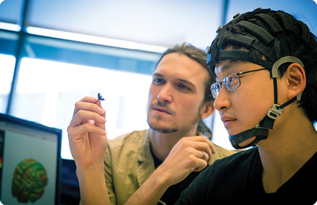 Mike Chi (right) wears the HD-72 Dry Wireless EEG Headset System, a series of connected bands outfitted with a built-in, wireless EEG amplifier and dozens of sensors, along with a small battery pack that sits at the neck. Here, Chi and engineer Tim Mullen take a closer look at one of the individual sensors. The headset is offered by San Diego-based Cogionics Inc., a spinoff company that grew out of technology developed at UCSD. Mullen now works at Syntrogi, another UCSD spinoff in the wearable sensor space working with Cognionics on the EEG signal processing side. (Photo courtesy of UCSD/Cognionics.)