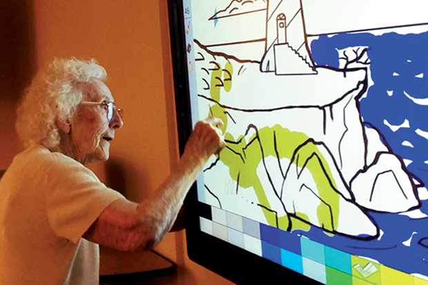 Figure 4: Front Porch began a trial with a scalable computer system in memory-care settings in June 2015 and, based on positive results, has since deployed more than a dozen units. Here, a resident uses her fingers to color on a 70-inch touchscreen television. Many other options are available for individual or group activities. (Photo courtesy of the Front Porch Center for Innovation and Wellbeing.)