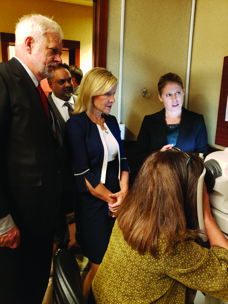 Figure 3. Abramoff (left) and Delaware Lt. Gov. Bethany Hall-Long (center) watch a demonstration of the IDx-DR system, which uses a robotic fundus camera and an artificial-intelligence algorithm to quickly diagnose DR. (Photo courtesy of IDx Technologies.)